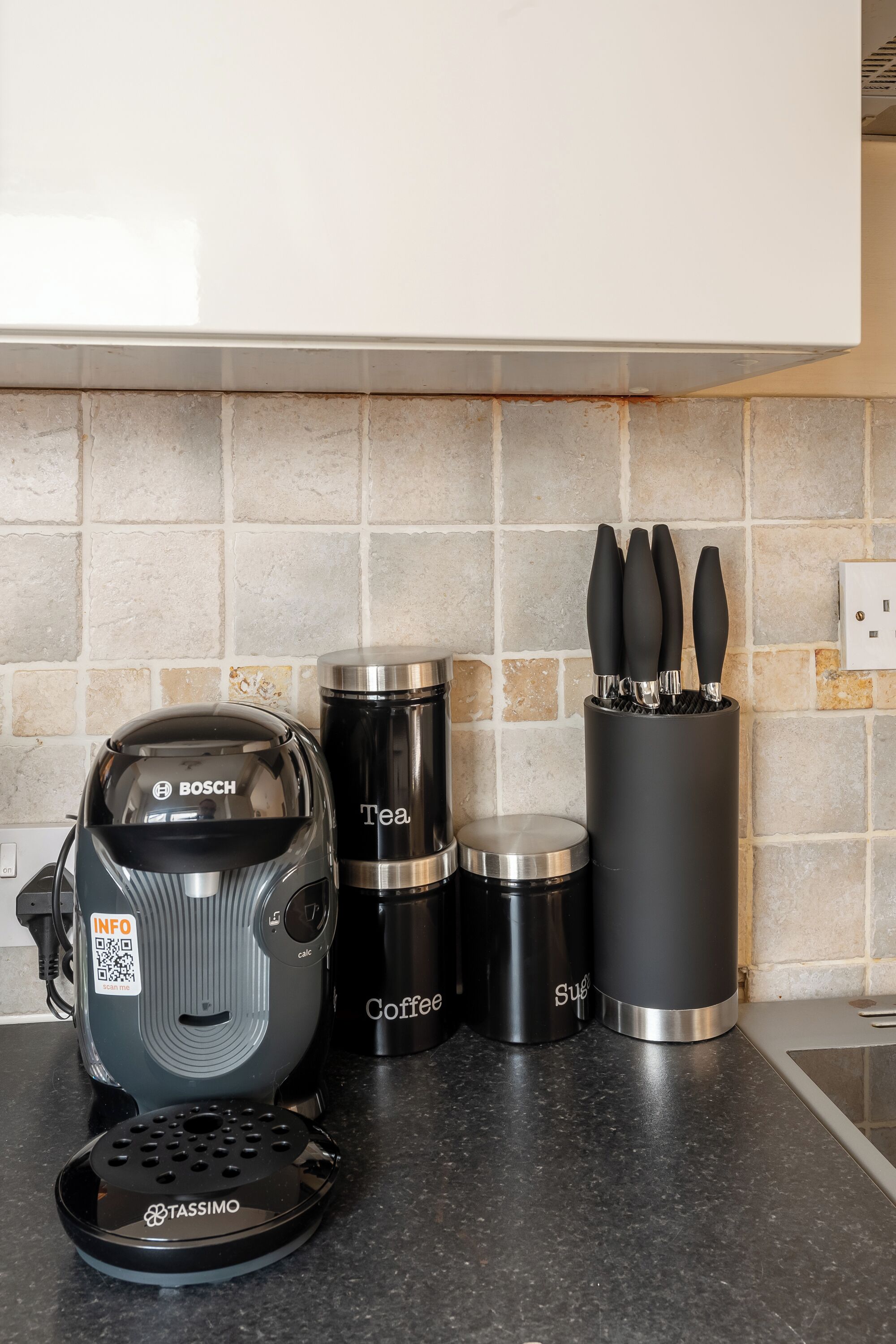 A kitchen with a Bosch coffee maker, a Tassimo pod dispenser, and two stainless steel containers labeled 'Tea' and 'Coffee.'