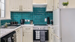 Una cucina compatta con mobili bianchi, uno schienale verde acqua, un forno nero e un frigorifero bianco.