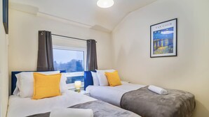 Camera d'albergo con due letti, una finestra con tende e un quadro incorniciato de 'La notte stellata' di Van Gogh, più un comodino con una lampada.