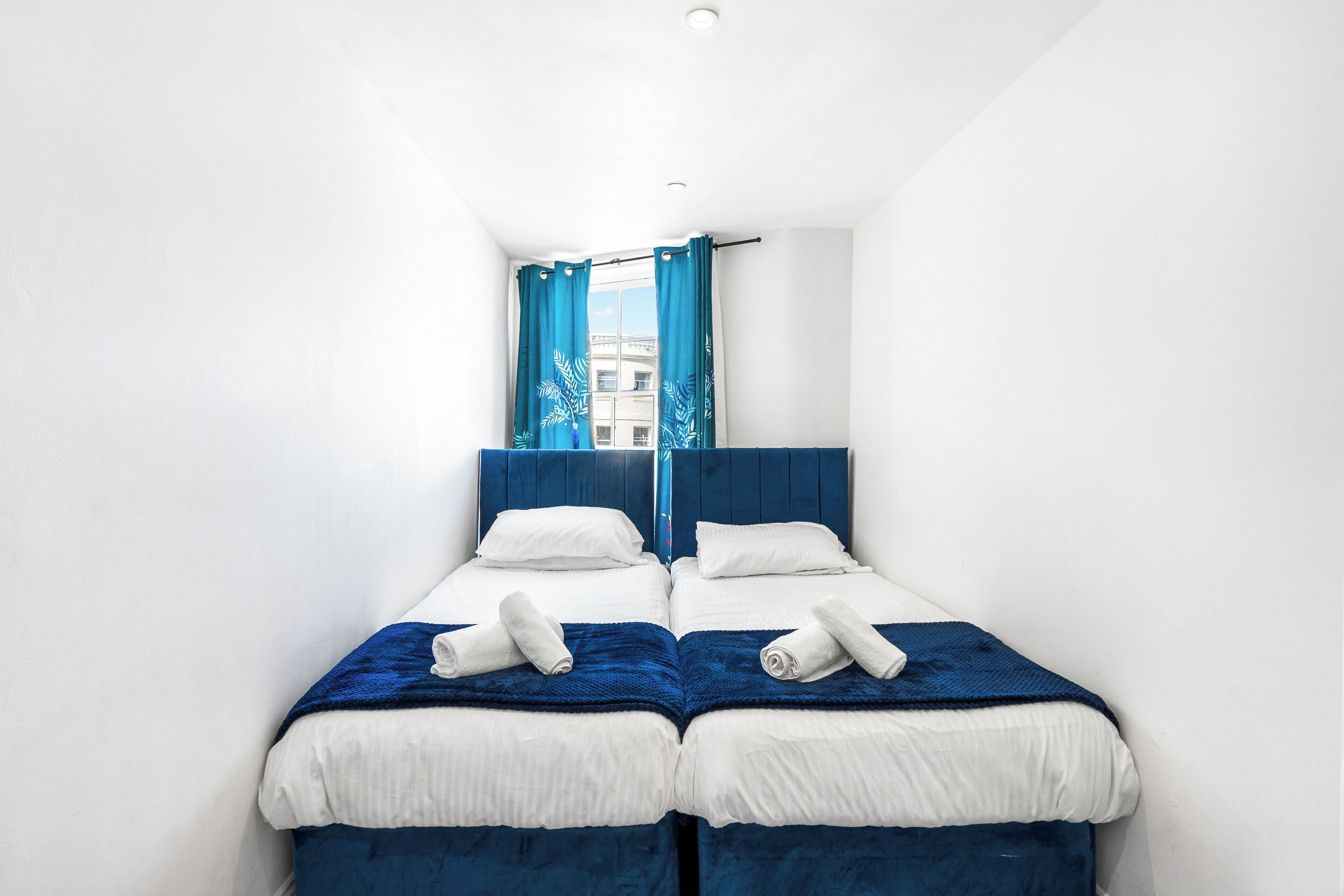 A twin room with two beds, a blue headboard, white bedding, and a window with blue curtains.