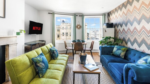 Ett modernt vardagsrum med en grön soffa, en blå soffa, ett soffbord och en tv-skärm som visar ”NETFLIX”.