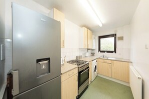 Eine kompakte Küche mit Kühlschrank, Herd, Backofen und Waschmaschine.