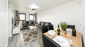 En moderne stue med sofa, sofabord og spiseområde med et bord dækket til to personer.