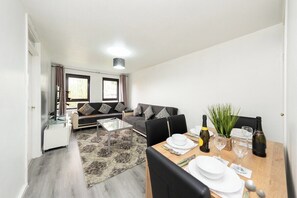 Ein modernes Wohnzimmer mit Sofa, Couchtisch und Essbereich, gedeckt für zwei Personen.