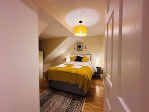 A bedroom with a bed, a nightstand, a lamp, and a patterned rug. - Cambridge | 3 BDR | Free Parking | Garden (Ely)