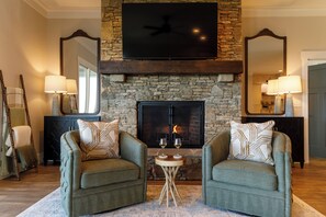 A living room with two armchairs, a fireplace, a flat-screen TV, and a stone wall.