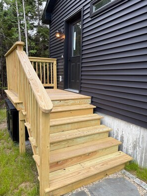 A wooden staircase leading to a black door, surrounded by a wooden deck and a metal railing. - Hidden Gem - NEW home in Southwest Harbor! (Southwest Harbor)