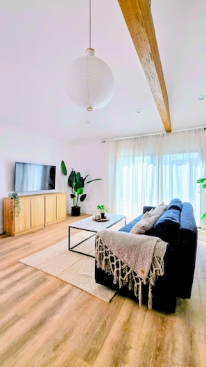 Ein modernes Wohnzimmer mit einer Couch, einem Couchtisch, einem Fernseher, einem Holzschrank und großen Fenstern.