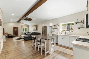 A spacious kitchen with a central island, white cabinetry, and a dining area with two chairs.