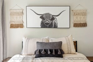 A bed with patterned bedding, a framed animal print, and macramé wall hangings.