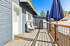 A wooden deck with two white chairs and a blue umbrella, a white door, and a white fence.