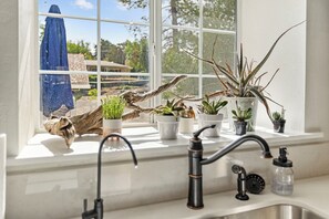 Eine Küche mit Fenster, Blumentöpfen und einem Wasserhahn.