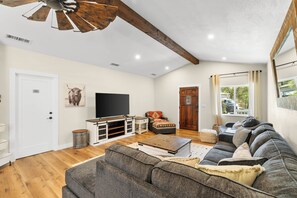 Uma sala de estar com sofá, mesa de centro, televisão e ventilador de teto de madeira.