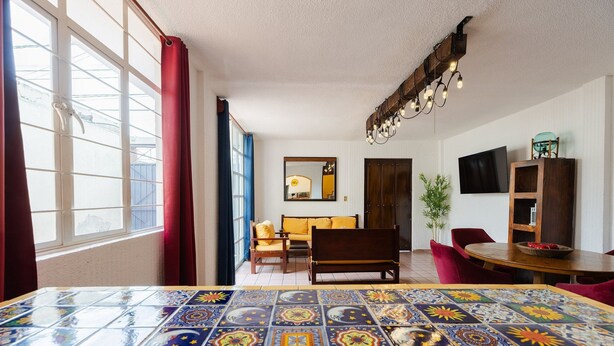A room with a large tiled floor, a sofa, a dining table, a TV, and a plant. - Casa San Pedro | Corazón de Cholula, Parking (Puebla)
