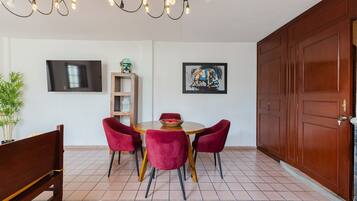Un coin repas comprenant une table ronde, quatre chaises, un banc, un téléviseur, une étagère et une porte.