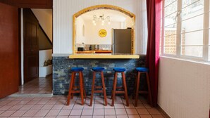 A kitchen with a stone countertop, wooden stools, a refrigerator, and a window with a curtain. - Casa San Pedro | Corazón de Cholula, Parking (Puebla)
