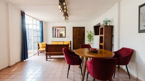 A dining area with a round wooden table, red chairs, a wooden cabinet, and a large window with curtains. - Casa San Pedro | Corazón de Cholula, Parking (Puebla)