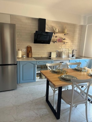 A modern kitchen with a built-in oven, a microwave, and a black range hood. There is a dining table with chairs and a white countertop with various kitchen items.