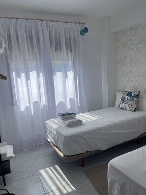 Une chambre à coucher comprenant un lit, une table de chevet, une chaise, une fenêtre avec des rideaux légers et un mur orné d’un motif floral.