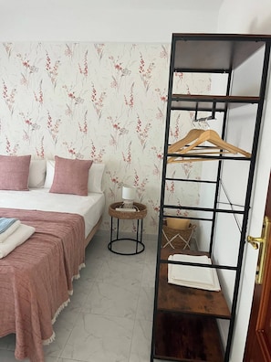 A bedroom with a bed, pillows, a bedside table with a lamp, a hanging rack, and a wardrobe.