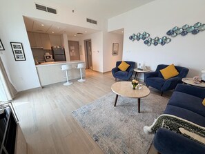 Ein modernes Wohnzimmer mit Sofa, Sessel und Couchtisch, im Hintergrund eine Küche und dekorative Wandbilder.