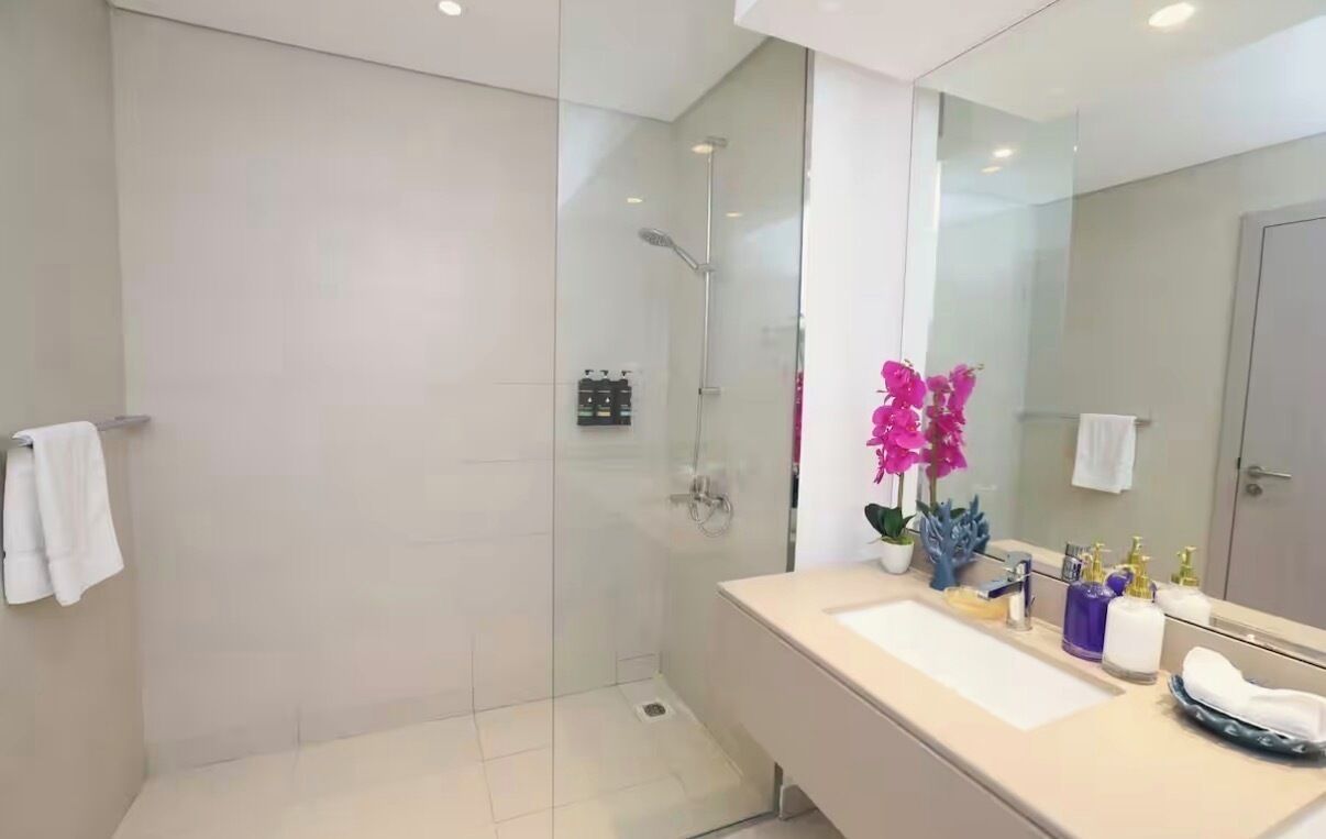 A modern bathroom with a glass-enclosed shower, a white sink, and a mirror.