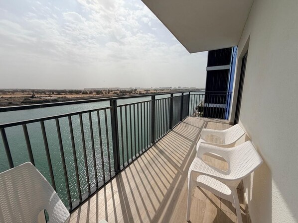 Ein Balkon mit Blick auf ein Gewässer und die ferne Landschaft, mit Tisch und zwei Stühlen.