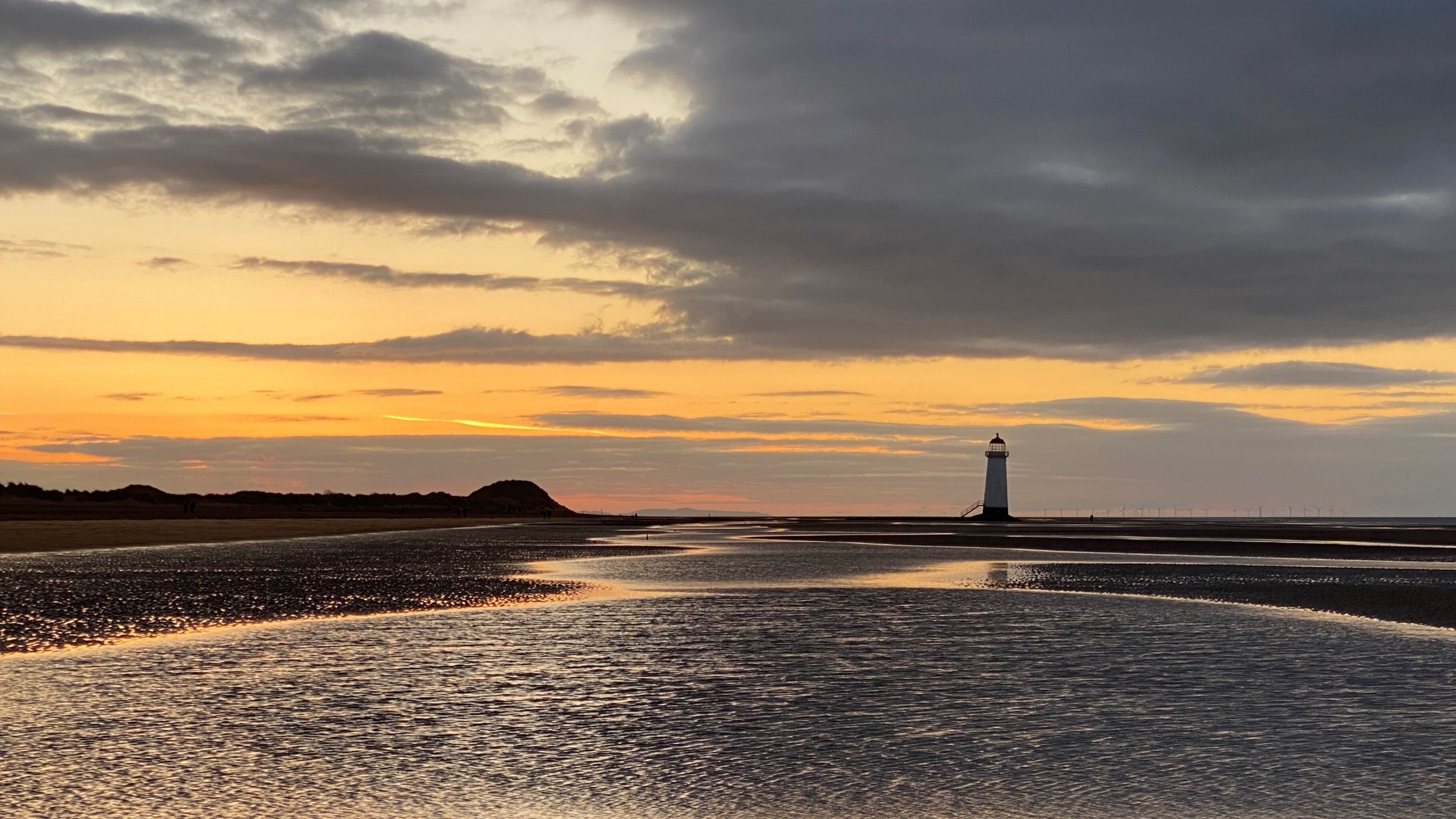 Een vuurtoren op een strand met een zonsondergang.