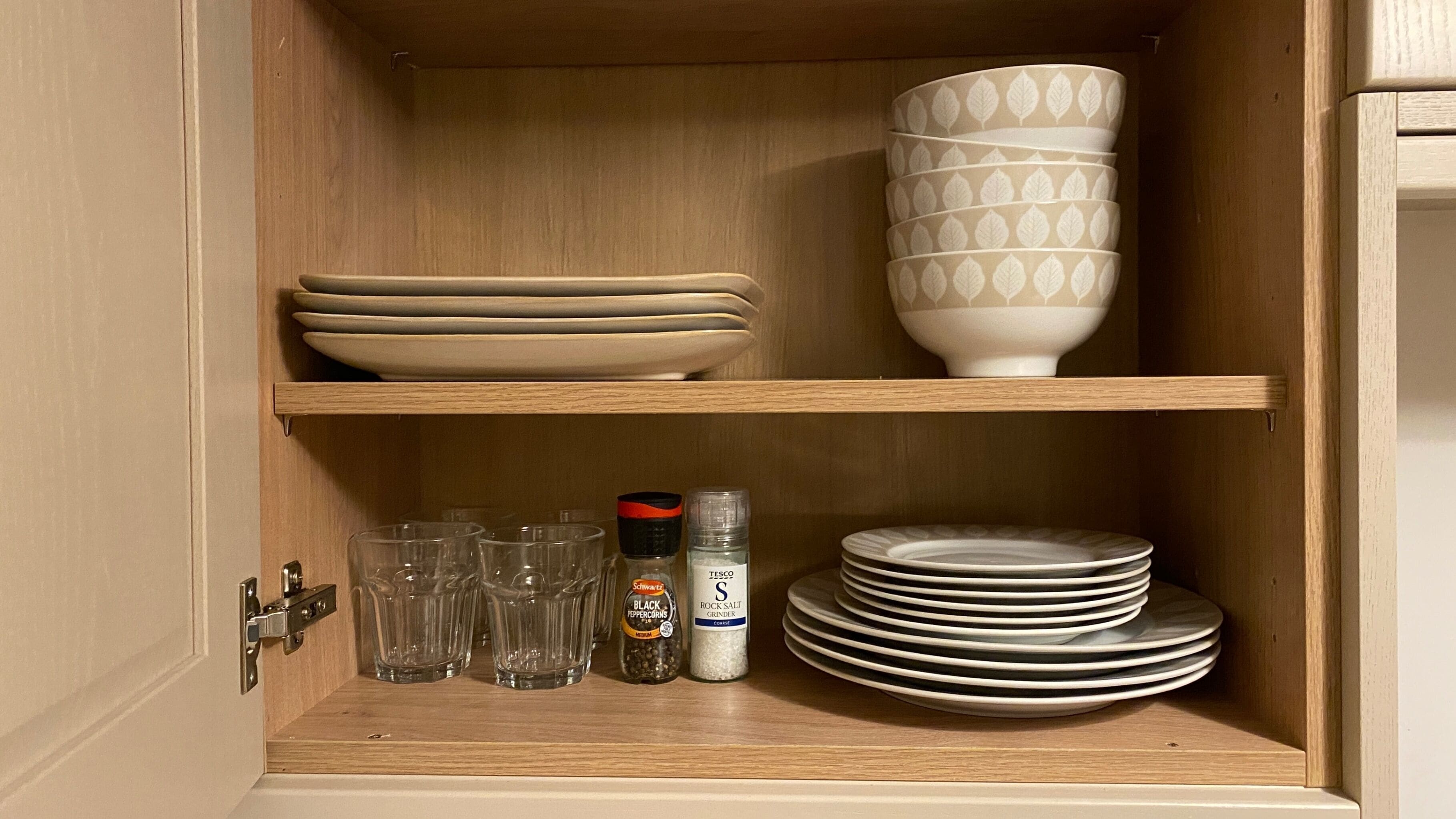 A wooden cabinet with shelves holding plates, bowls, glasses, and salt containers.