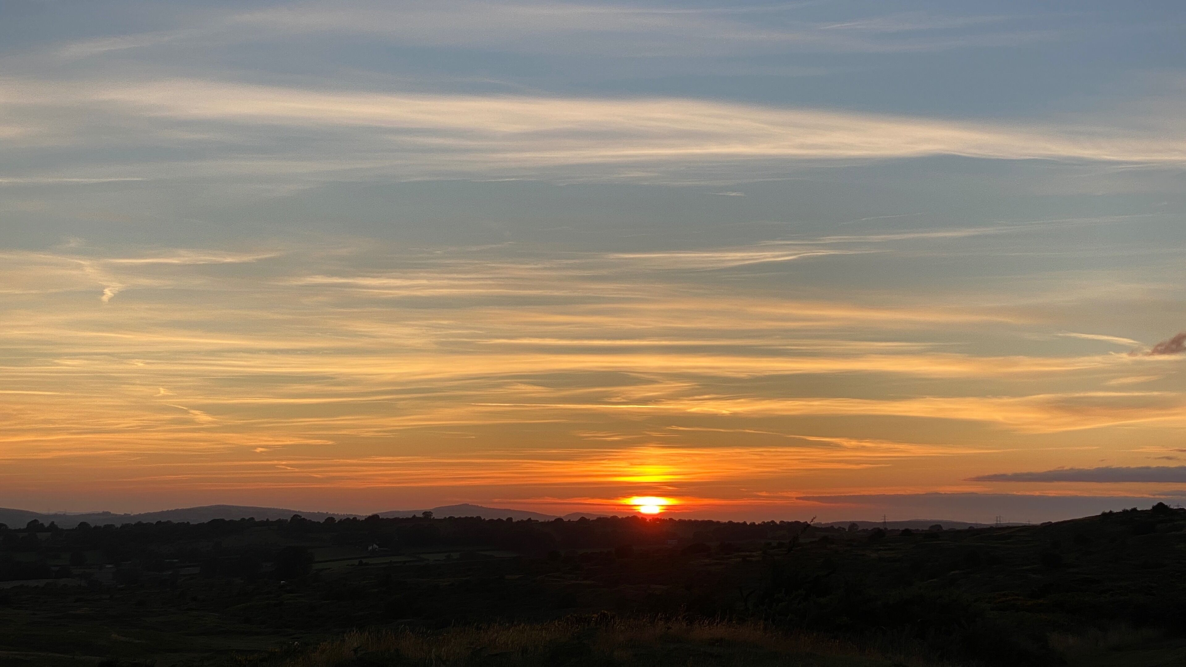 Un atardecer sobre un paisaje rural con cielo despejado y colinas distantes.