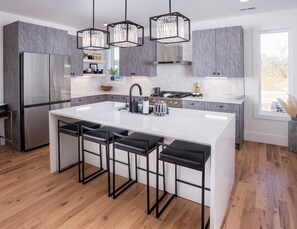 A modern kitchen with a central island, bar stools, a refrigerator, and pendant lights. - Private Rooftop Hot Tub & Cabana @TheNewCumberland (Nashville)