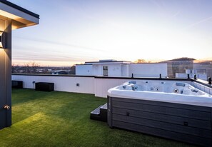 Une terrasse sur le toit équipée d’un jacuzzi, recouverte de gazon synthétique, et offrant une vue dégagée sur les toits de la ville.