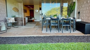 A modern patio with a dining table and chairs, a sofa, and a large window overlooking a garden. - Surf Rider, Newly Remodeled, Walk Out Lanai, Ocean View, 2ACs, 350Steps to Kam 1 (Kihei)