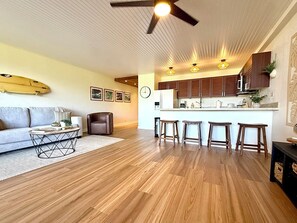 A modern living room with a sofa, coffee table, and a dining area with bar stools. - Surf Rider, Newly Remodeled, Walk Out Lanai, Ocean View, 2ACs, 350Steps to Kam 1 (Kihei)