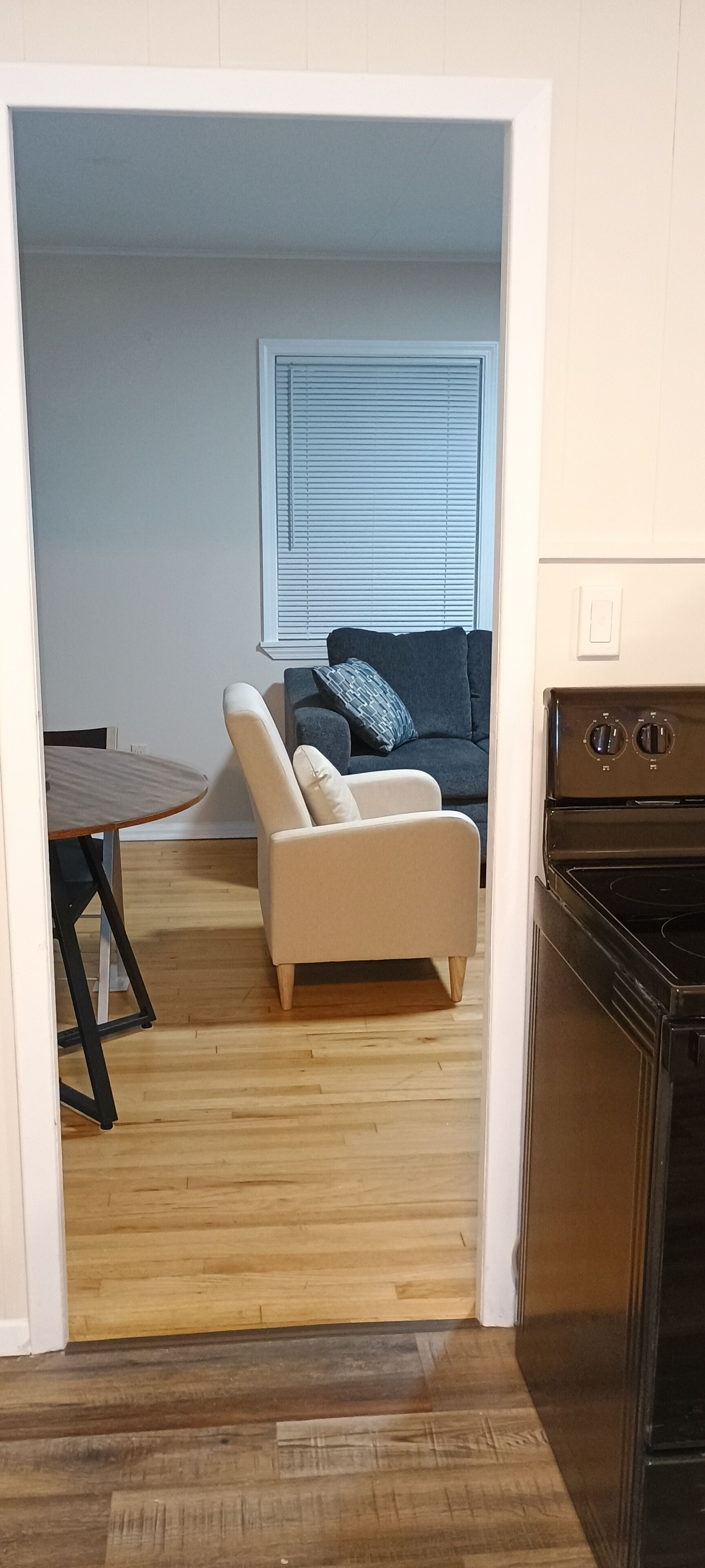 Een keuken met een fornuis, een eettafel met stoelen, een bank en een raam met jaloezieën.