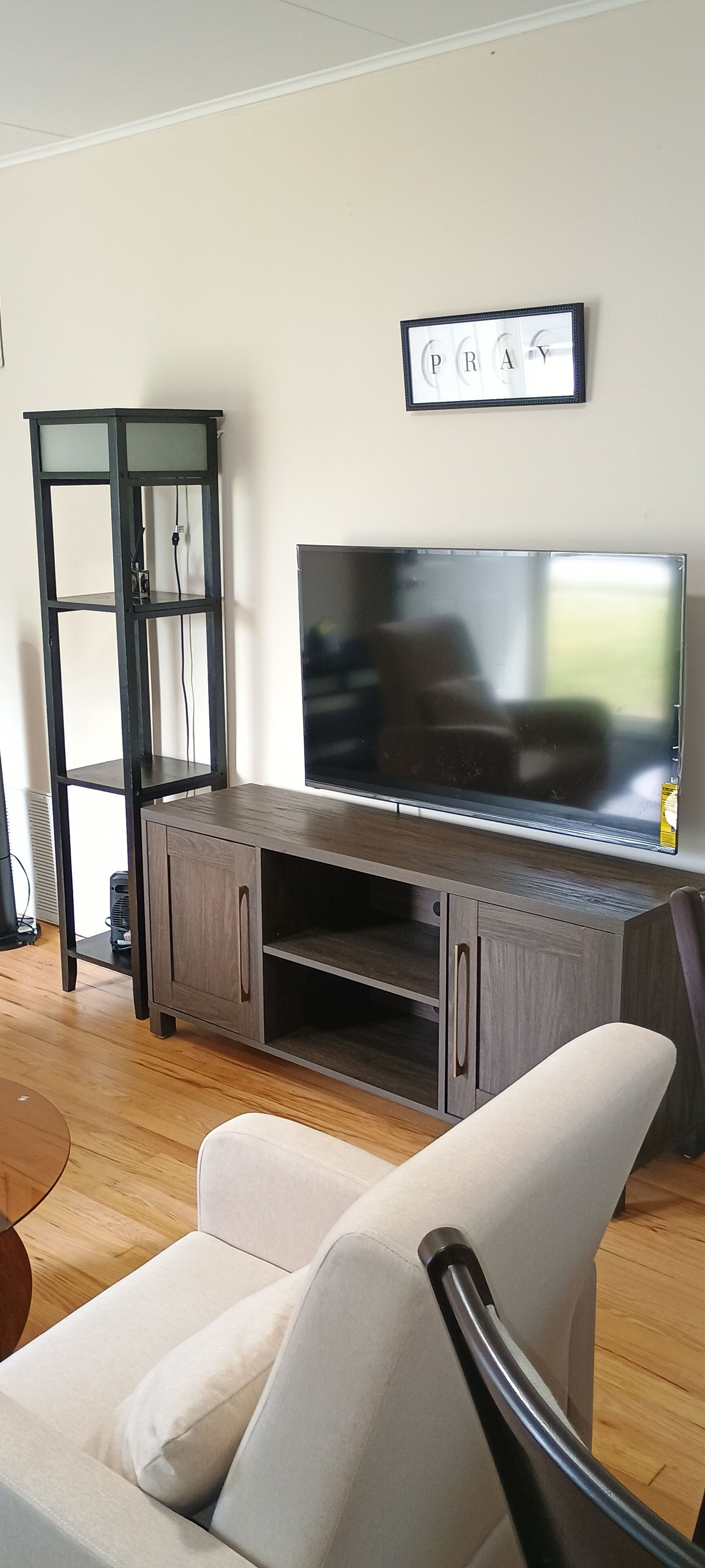 Un salón con televisor sobre un mueble de madera, un sofá blanco y una estantería negra.