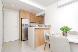 Eine moderne Küche mit Holzschränken, einem Edelstahl-Kühlschrank und einer kleinen Kochinsel mit weißer Arbeitsplatte.