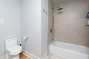 Et badeværelse med toilet, bruser og badekar.