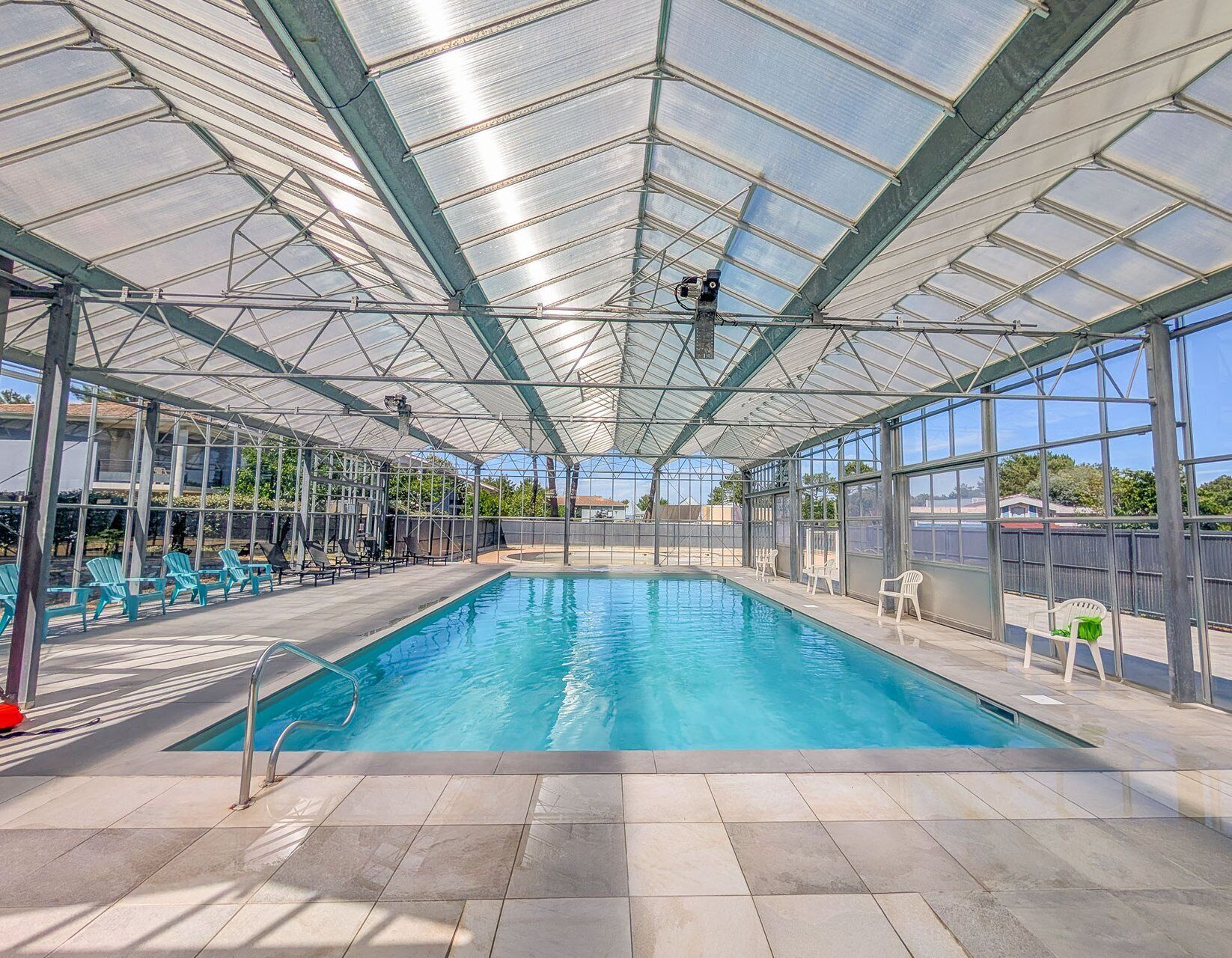 A covered swimming pool with clear blue water, surrounded by chairs and a glass ceiling structure.. L'Escale de l'Estuaire, T3 with Pool Near Soulac