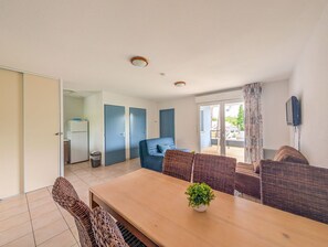 Une pièce comprenant une table à manger, des chaises, un canapé, une petite plante, un téléviseur et une vue sur l’extérieur.