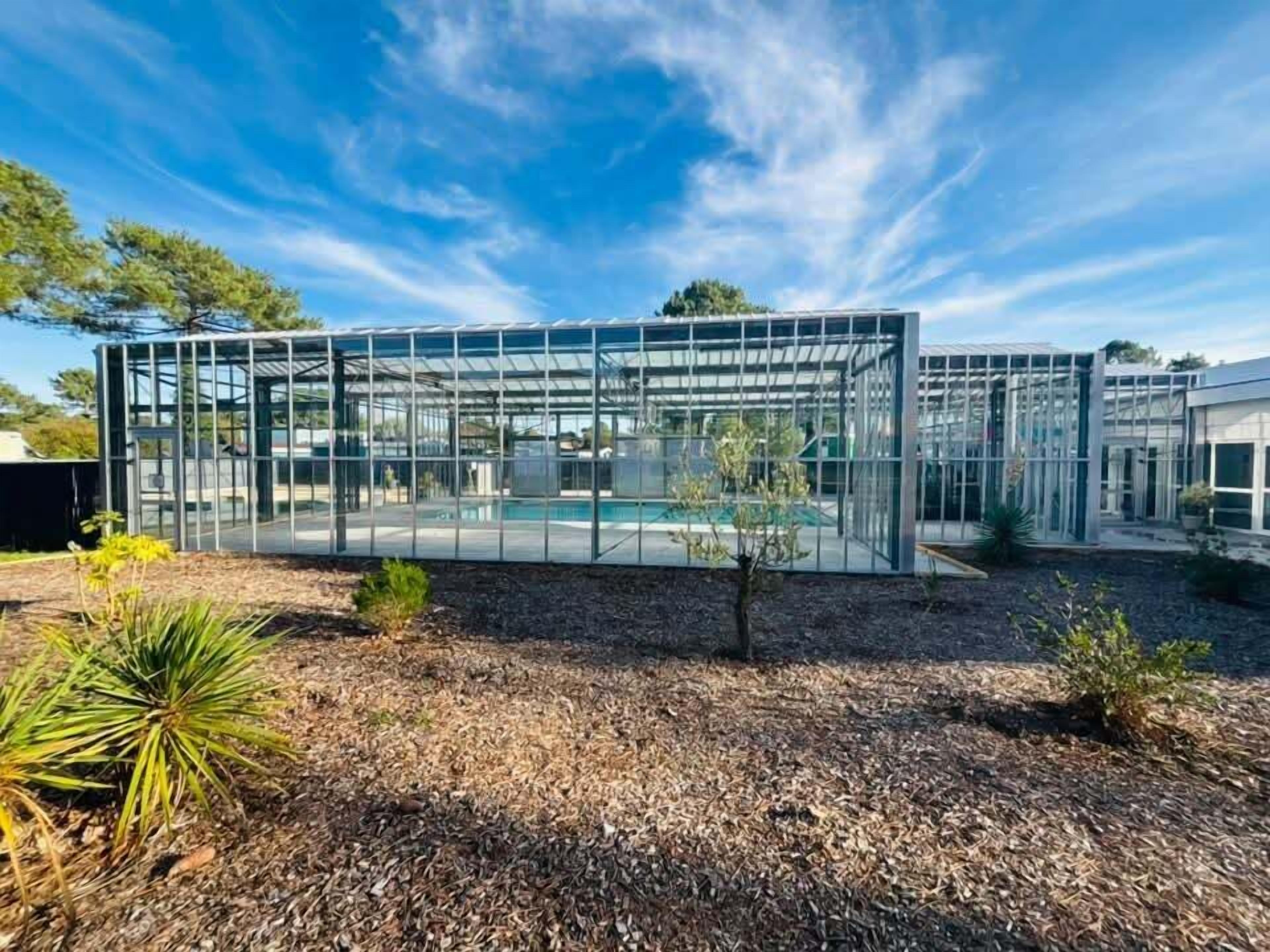 A modern glass structure with a pool, surrounded by a landscaped area with mulch and small plants.