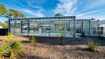 Une structure moderne en verre, dotée d’une piscine, et entourée d’un espace paysager agrémenté de paillis et de petites plantes.