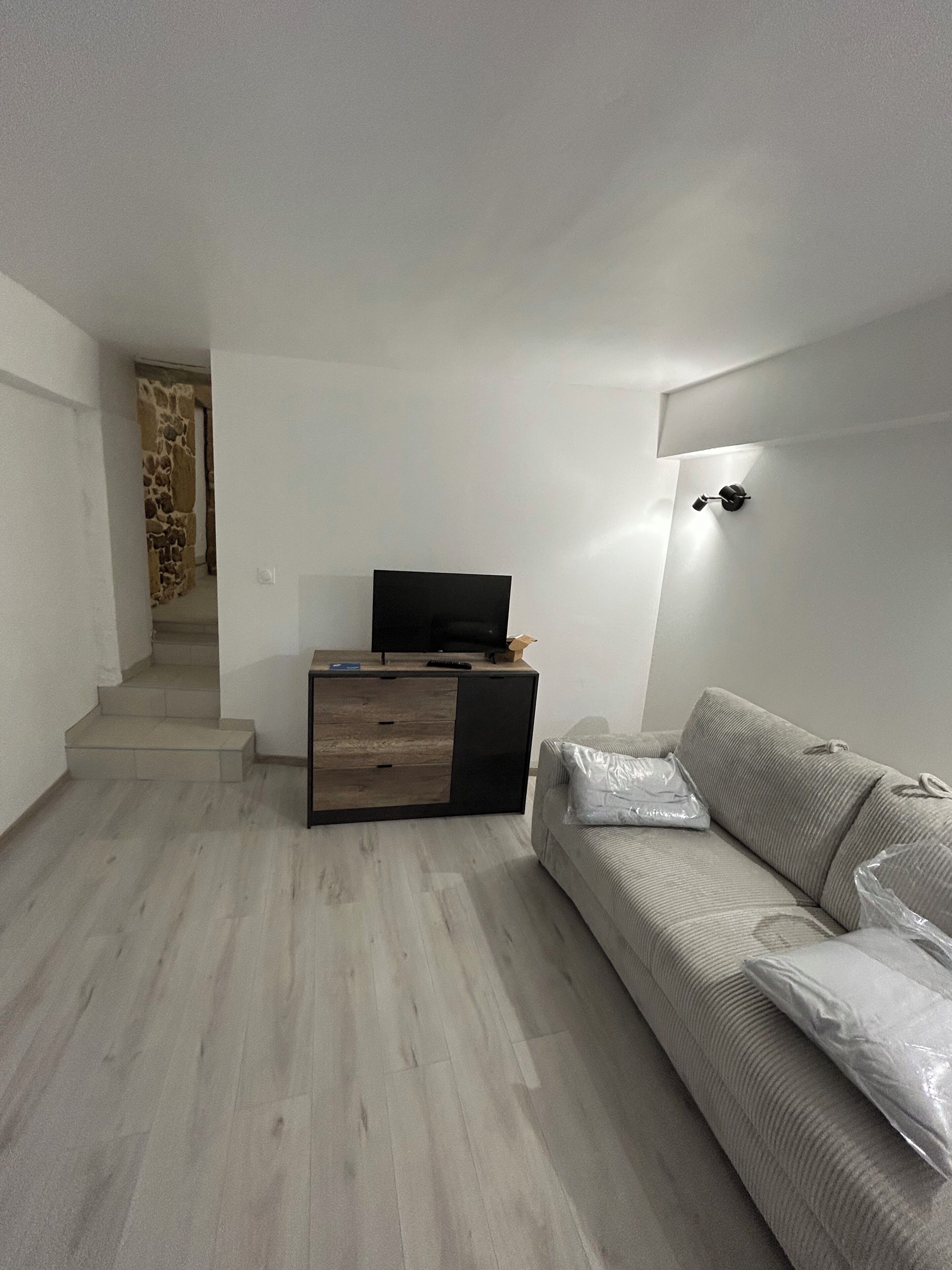 A modern living room with a sofa, a TV on a wooden cabinet, and a staircase leading to another room.