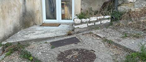 A building entrance with a door, a small step leading up, and a manhole cover on the ground.