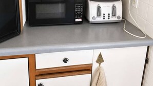 A kitchen with a microwave, toaster, and a wooden shelf above the countertop. - The only direct-waterfront home at Anchorage — 2BR, 2BA, and lake views from every room. (Iosco County)