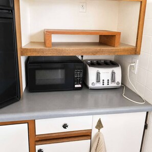 Une cuisine équipée d’un four à micro-ondes, d’un grille-pain et d’une étagère en bois au-dessus du plan de travail.