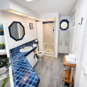 Een badkamer met een blauw betegeld wastafelmeubel, een douche en een toilet.