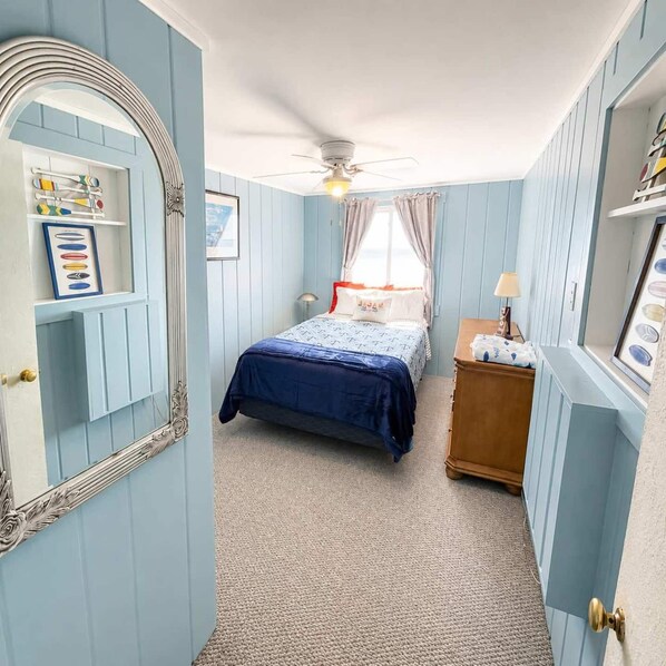 Un dormitorio con cama, mesita de noche, espejo y ventilador de techo.