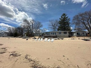 Een strandhuis met een zandige voortuin, een groot raam en uitzicht op de lucht.