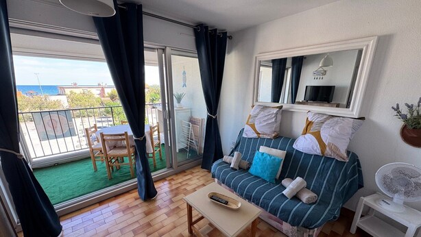 Et værelse med sofa, bord, stol, balkon med udsigt og ventilator.